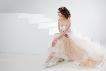 Bride sits on the stairs. Portrait of a beautiful girl in a wedding dress. Dancing Bride, white background. © Ulia Koltyrina