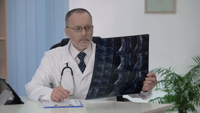Spinal surgeon examining backbone mri, making notes in patient's medical card