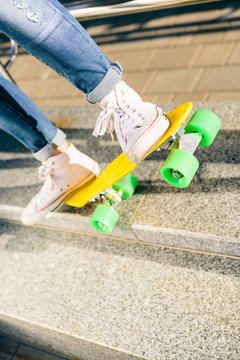 Close up of sport lady's legs in jeans and white sneakers on penny board skateboard. Modern urban hipster girl have fun. Good sunny summer day for lifestyle skateboarding and have fun.
