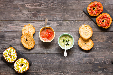 Italian bruschetta with cheese, tomato sauce, cucumber sauce, and herbs, on a wooden background.