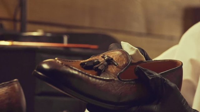 Close up of cobbler mans hands in gloves polishing a leather shoe at workshop