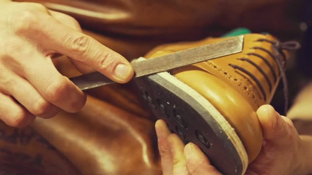 Close up of bootmaker hands repairing a shoe with a file at the workshop