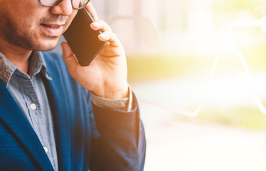 Handsome businessman in suit and eyeglasses speaking on the phone in office,Side view shot of a man's hands using smart phone in rear view of business man busy using cell phone at office.