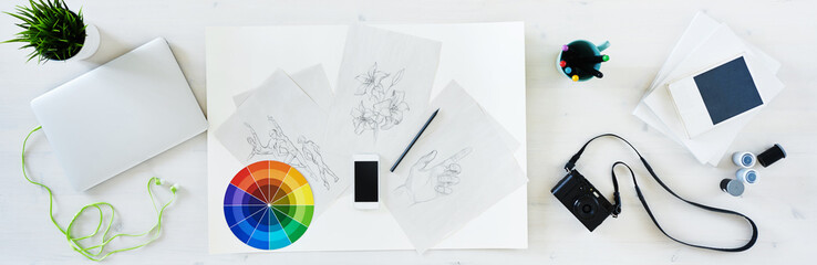 Obraz premium Aerial view of designer desk with creative tools: laptop, camera, film, sketches, phone, etc