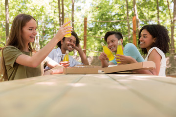 Cheerful young multiethnic friends students outdoors drinking juice eating pizza