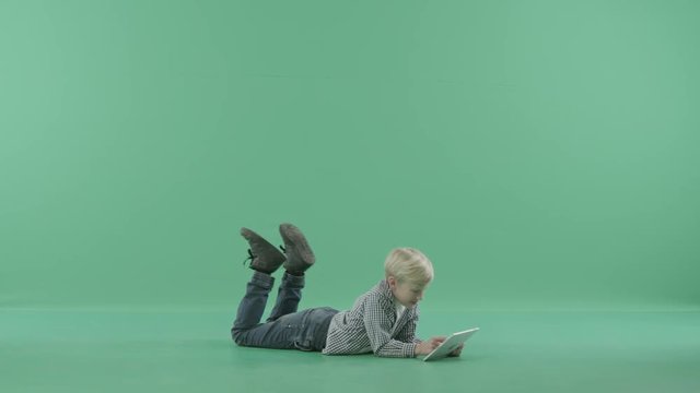 Boy lies on the floor and swings legs using his tablet computer