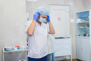 Fototapeta premium Handsome mature surgeon in blue medical wear and mask is putting on medical gloves at operating room