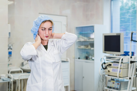 Young doctor during preparation for operation. Assistant of surgeon wearing medical cap in operation room at the hospital. Female surgeon attaching his mask in an operating theater.
