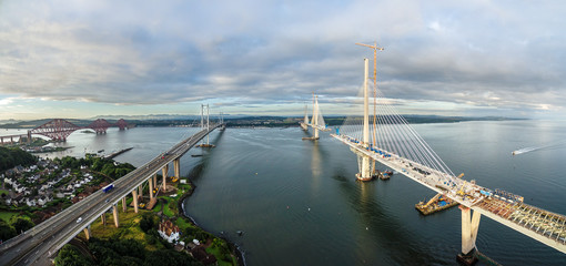 The new Queensferry Crossing bridge (on the right) under construction over the Firth of Forth with the older Forth Road bridge (on the left) and with the iconic Forth Rail Bridge in the far left.