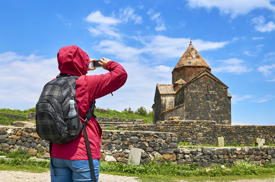 Woman with backpack taking photo of ancient monastery
