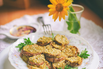 Rustic dinner with fried zucchini slices with nut sauce and greens. A white plate with food stands on a lacy rustic tablecloth, a bouquet with flowers in the background. Selective focus