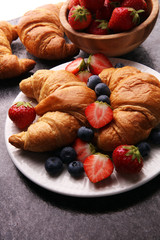 Delicious breakfast with fresh croissants and ripe berries on old marble background