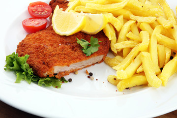 Dish of Wiener schnitzel and French fries served with sauces and salad on rustic wooden table