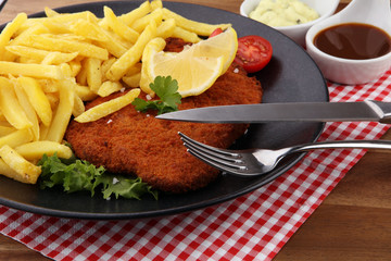 Dish of Wiener schnitzel and French fries served with sauces and salad on rustic wooden table