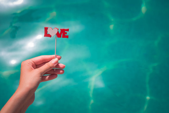 Close up of female holding stick with love sign against blue water surface
