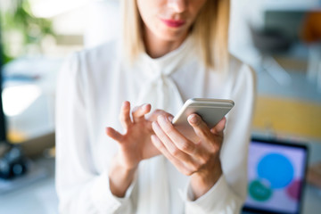 Businesswoman in her office with smartphone texting.