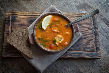 Marmitako soup in a ceramic bowl on a wooden board, next to a piece of bread