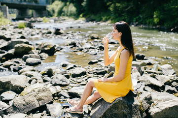 Travel in mountains. River with stones on shore. Heat temptation. Thirst suffer. Young girl drinking water. Satisfaction of wish.  Eyes closed in peace and harmony.  Rest in pleasure.  Tired under sun