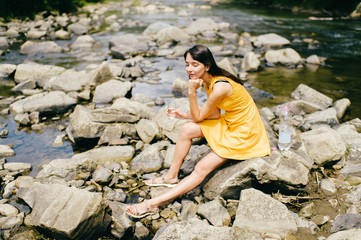 Travel in mountains. River with stones on shore. Heat temptation. Thirst suffer. Young girl drinking water. Satisfaction of wish.  Eyes closed in peace and harmony.  Rest in pleasure.  Tired under sun