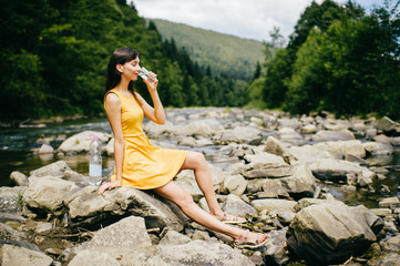 Travel in mountains. River with stones on shore. Heat temptation. Thirst suffer. Young girl drinking water. Satisfaction of wish.  Eyes closed in peace and harmony.  Rest in pleasure.  Tired under sun