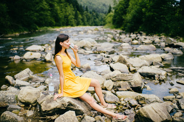 Travel in mountains. River with stones on shore. Heat temptation. Thirst suffer. Young girl drinking water. Satisfaction of wish.  Eyes closed in peace and harmony.  Rest in pleasure.  Tired under sun