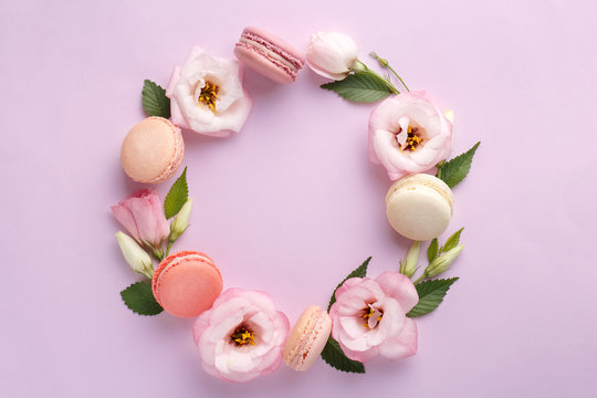 Naklejki Macarons and flowers wreath on a purple background. Colorful french dessert with fresh flowers. Top view