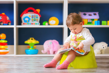 Cute little baby girl,sitting on potty and reading.