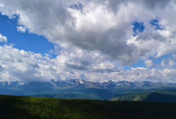 Obraz premium View of snow peaks of North-Chuyski ridge, green hills and blue sky with clouds in Altai mountains. Altay Region, Siberia, Russia.