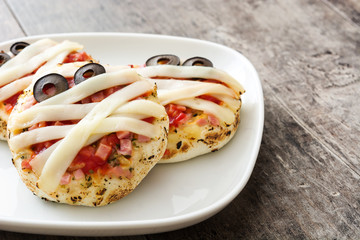 Halloween mummies mini pizzas on wooden table.
