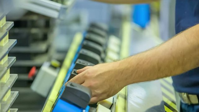 A young man is attaching something with another tool. There are lots of the same type of products down the conveyor belt.