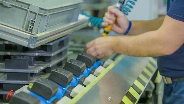 A young man is attaching something with a tool on all the products down the conveyor belt. 