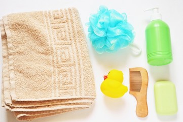 Flat lay toiletries kit/ Beige cotton towel, blue sponge, yellow toy rubber duck, green liquid soap and wooden comb. Bath products for baby. Top view photo