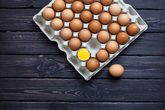 Top view of chicken eggs in a cardboard box on a dark wooden table with copy space.