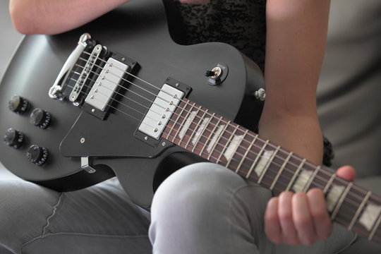 Frau hält schwarze E-Gitarre - Ausschnitt