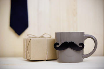 Tie, gift box, paper mustache, coffee cup on wooden background with copy space. Greetings and presents. Happy Father's Day.