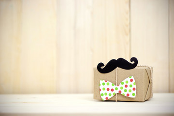 Gift box, paper mustache, tie on wooden background with copy space. Greetings and presents. Happy Father's Day.
