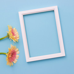 Photo frame and yellow flower on bright blue wooden background with petals. Summer flat lay.