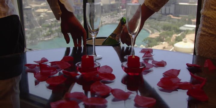 Slow motion of couple holding hands. Rose petals and champagne by them.
