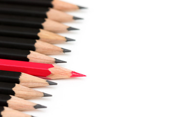 Red pencil standing out from crowd of plenty identical black fellows on white table. Leadership,...