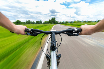Rider driving bicycle on an asphalt road. Two hand on bike handlebar. Motion blurred background