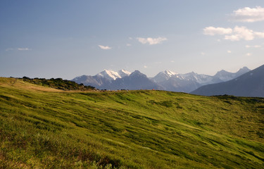 Fototapeta premium Mountain ranges and snow peaks with alpine meadow hiking camp of tents in the foreground under blue sky and white clouds Altai Mountains Siberia, Russia