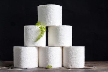 Stack of toilet paper rolls on wooden table against black background. Copy space.