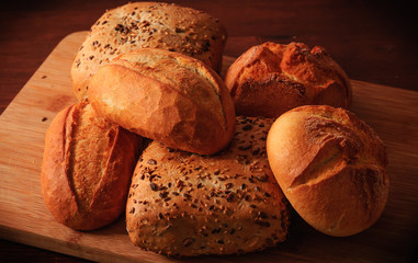 Wheat rolls and multigrain rolls on a wooden board and a brown table