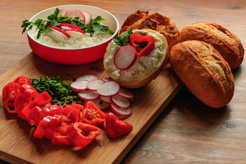 Healthy breakfast with cream cheese, buns and vegetables on a brown table