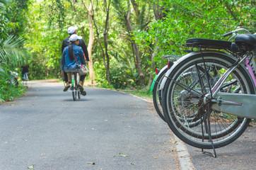 bicycle wheel parking on the asphalt road side in park and peaple ride a bicycle.