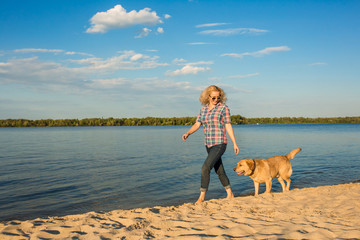 Happy young woman walking along a beach with her golden retriever at the sunset