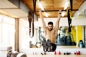 Fitness man hanging on horizontal bar performing legs raises, in the gym.