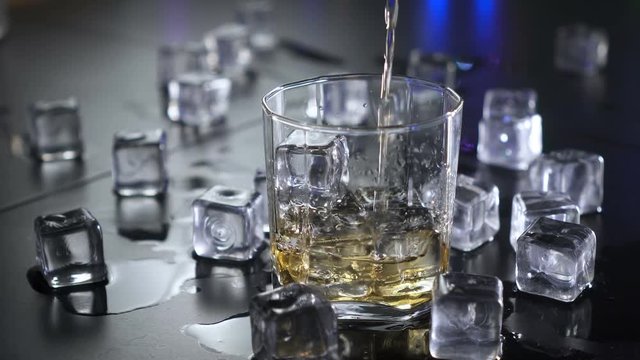 Close up pouring whiskey to glass over ice cubes. UHD 4k 3840x2160.
