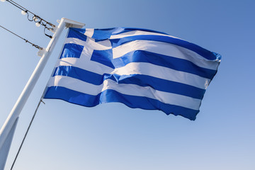 Greek national flag waving on the wind against blue sky.
