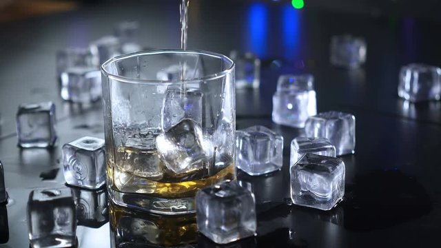 Close up pouring whiskey to glass over ice cubes. UHD 4k 3840x2160.
